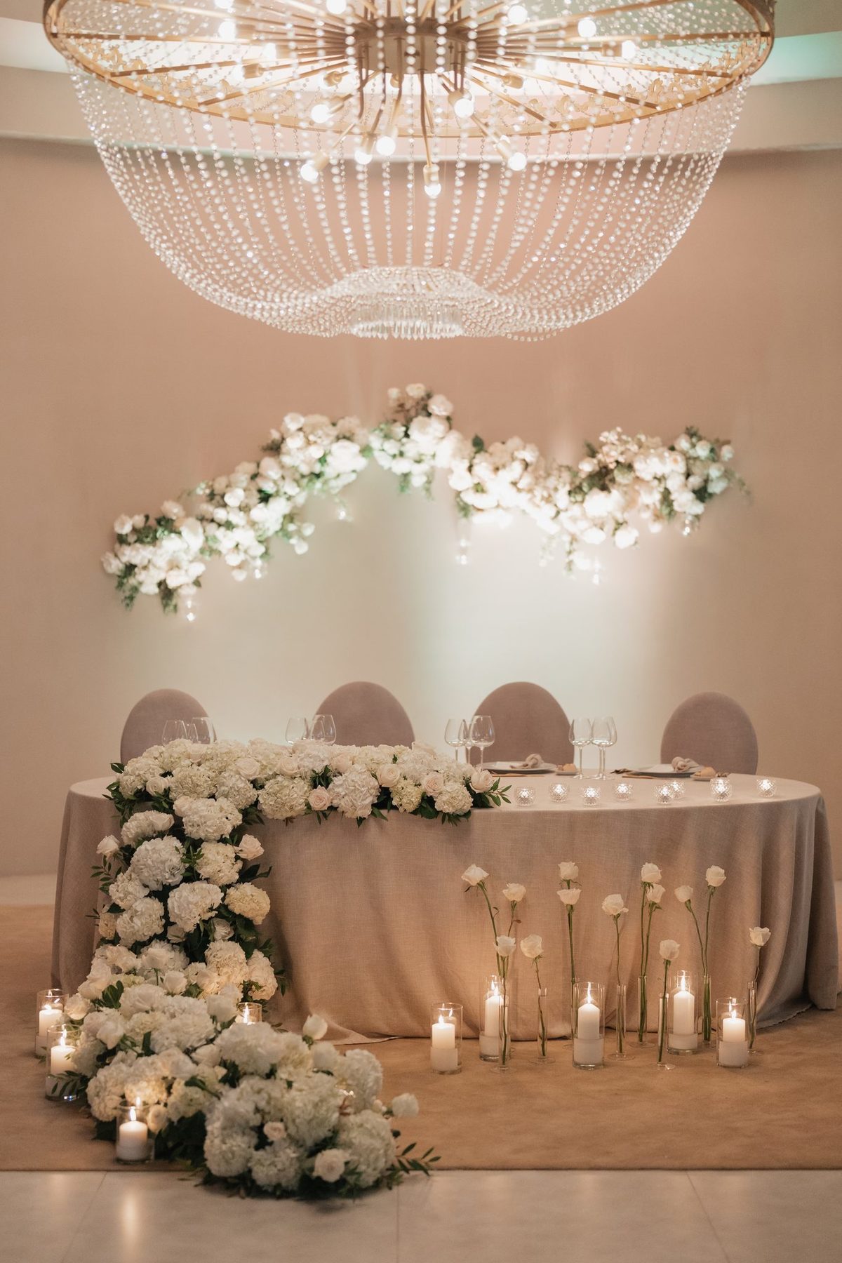 Mesa dos noivos sob lustre de cristal com cascata de flores brancas e velas