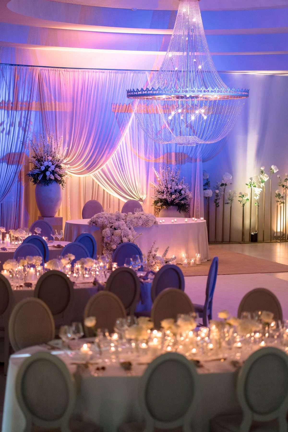 Sala com cortinados, lustre de cristal e mesas redondas iluminadas