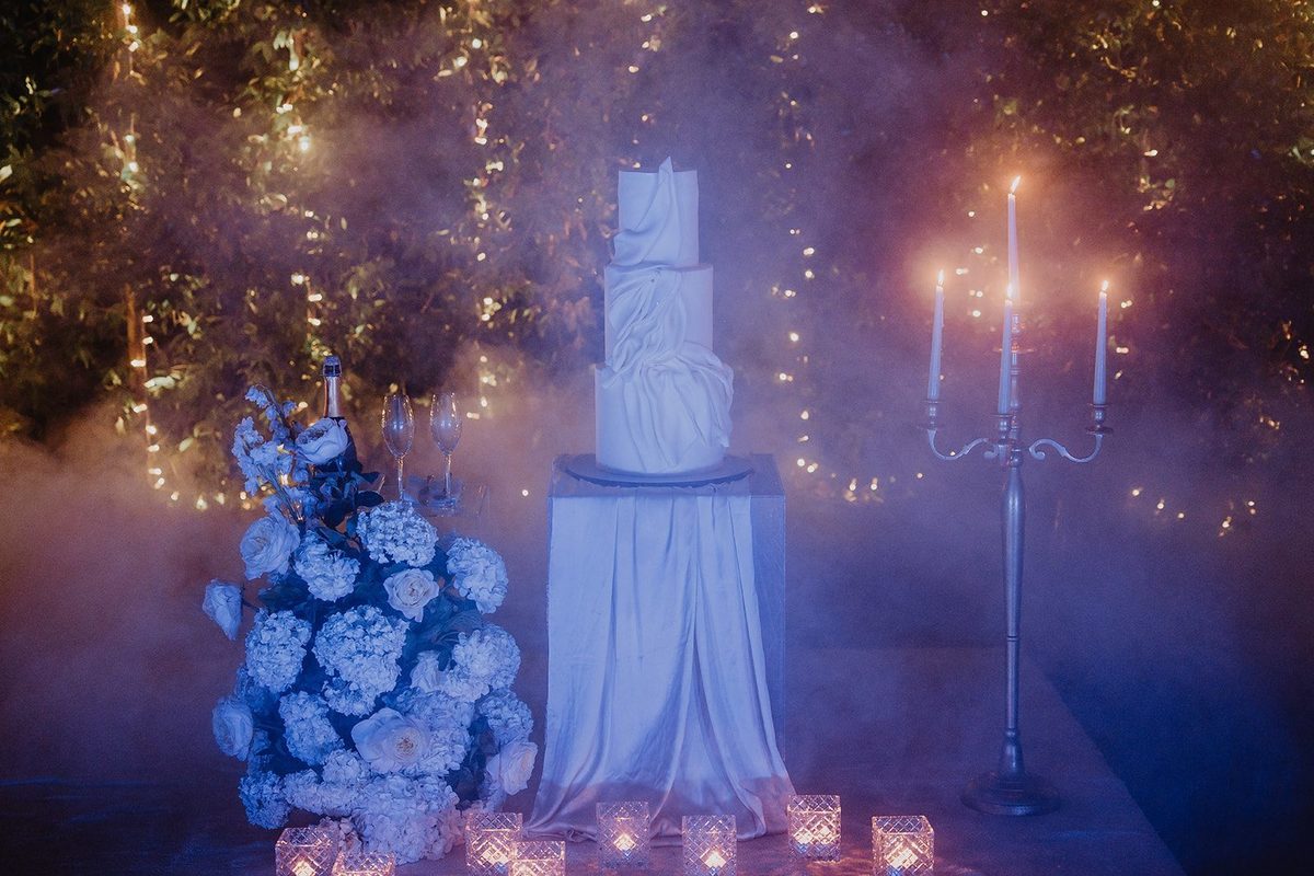 Bolo de noiva branco com hortênsias azuis, candelabros e fumo baixo à noite
