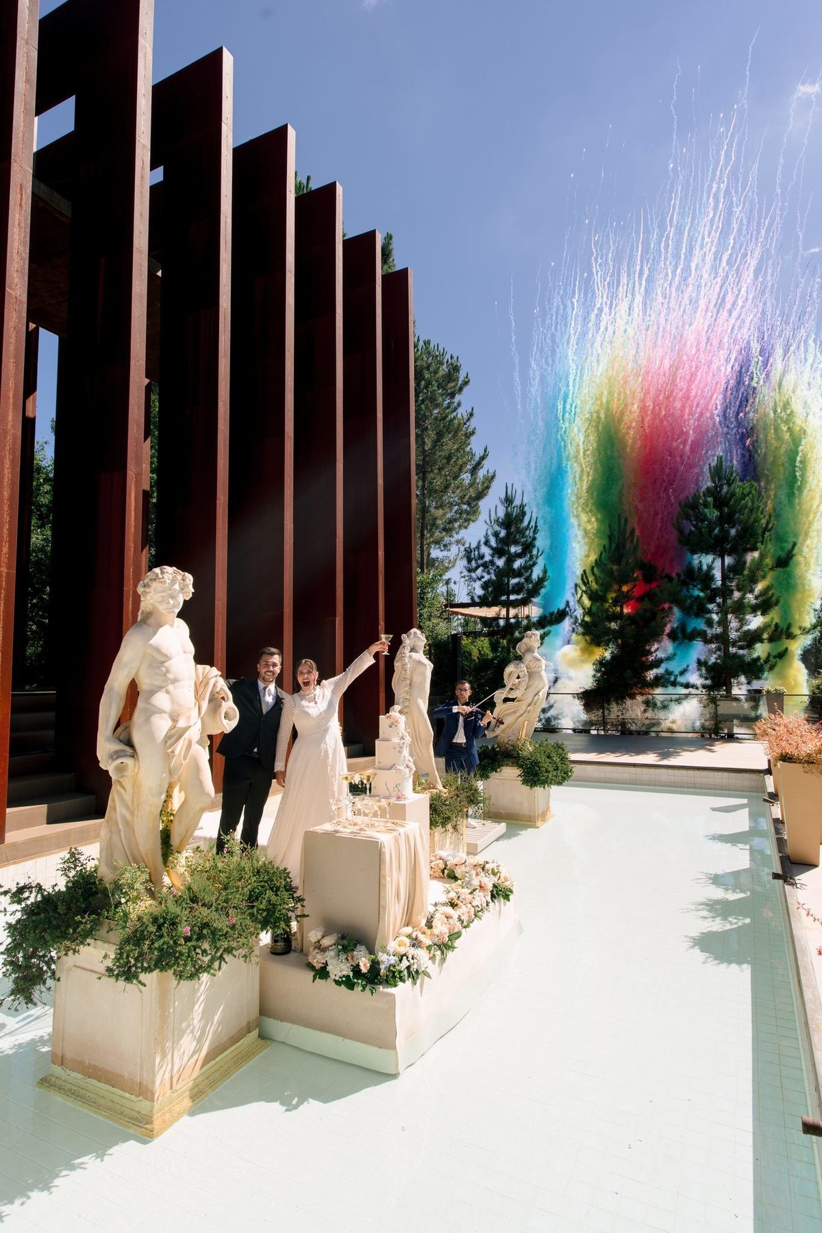 Noivos a celebrar com fumo colorido entre as estátuas e a arquitetura em aço corten