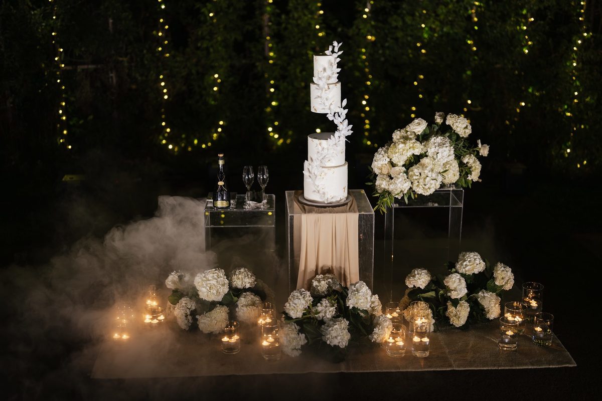 Bolo de noiva em pedestal com hortênsias brancas, velas e fumo baixo