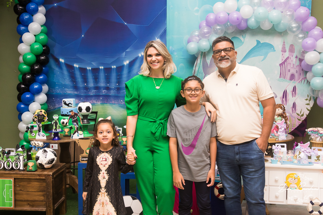 família com pai, mãe, filho e filha em frente a duas mesas decoradas para festa