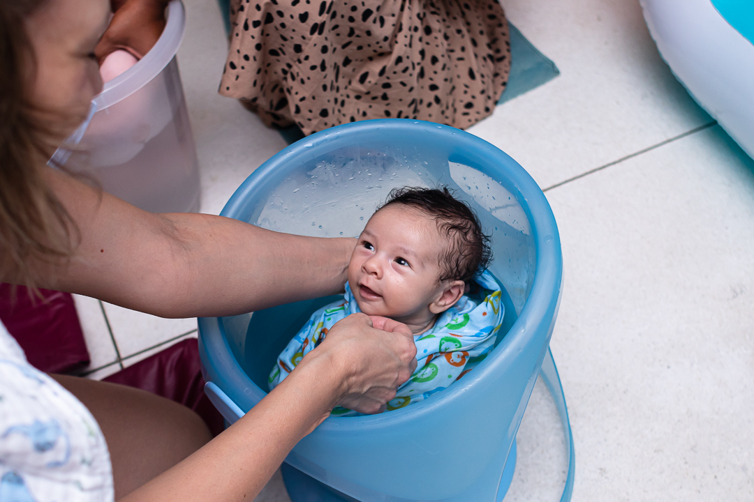 bebe enrolado em cueiro em banho de balde sorrindo para a mãe