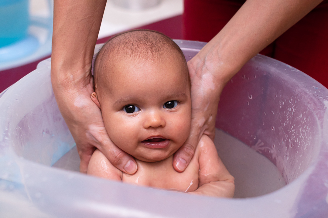 bebe em balde tomando banho de ofurô sendo segurada pelo pai