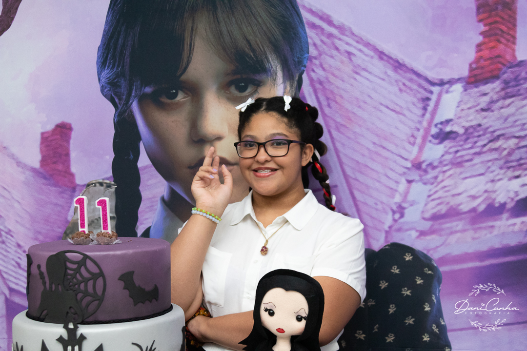 menina fazendo pose da Wandinha em mesa decorada com o mesmo tema