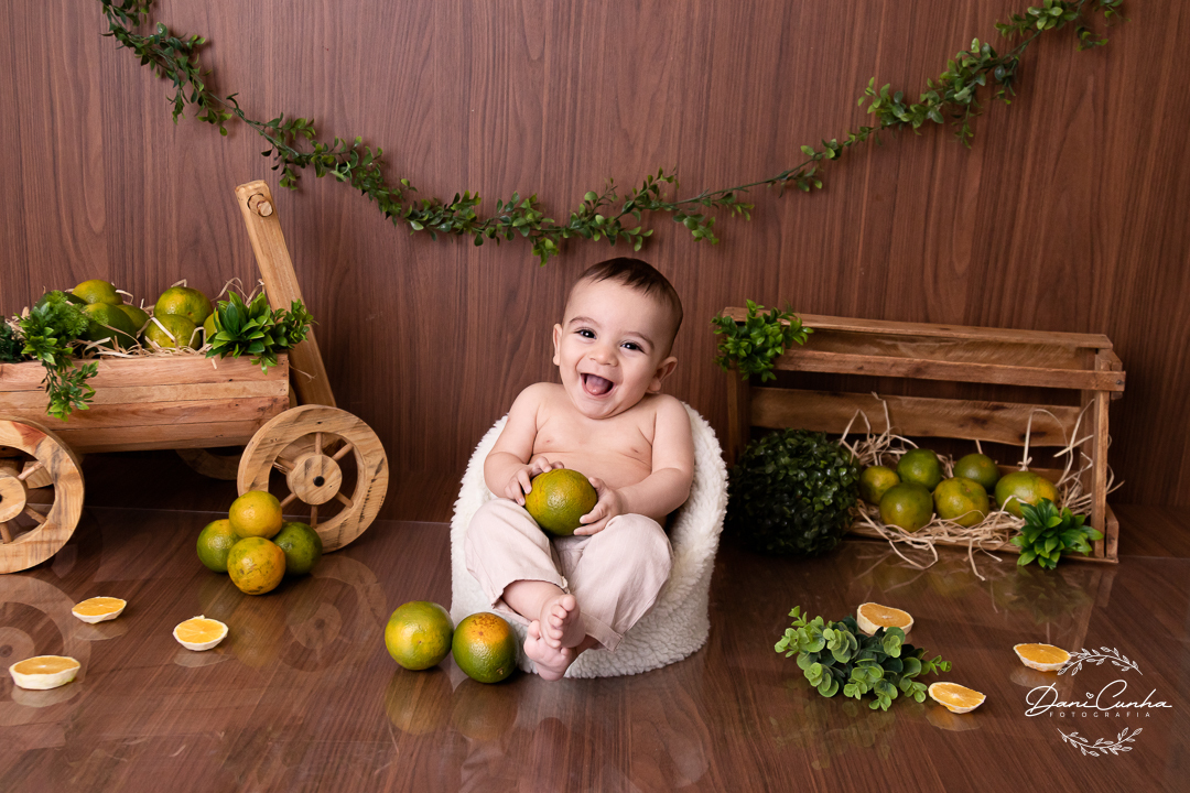 bebe sentado em poltroninha com cenario com laranjas, e segurando laranja na mão