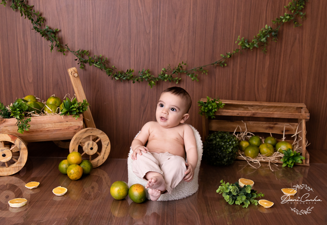 bebe sentado em poltroninha com cenario com laranjas, olhando para o lado