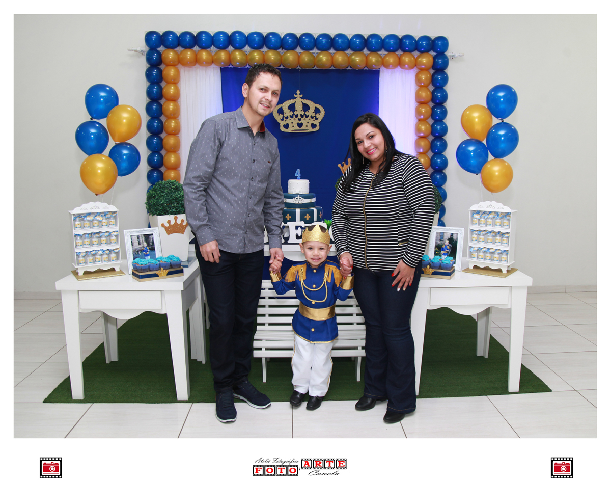 aniversariante em pé com os pais na frente da mesa do parabéns