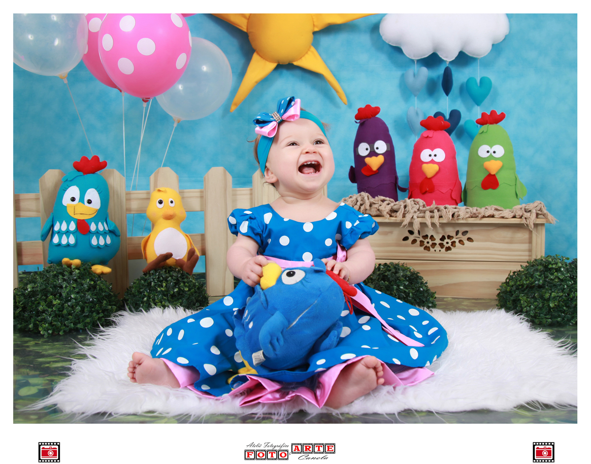 menina de vestido azul sorrindo sentada com a galinha pintadinha no colo