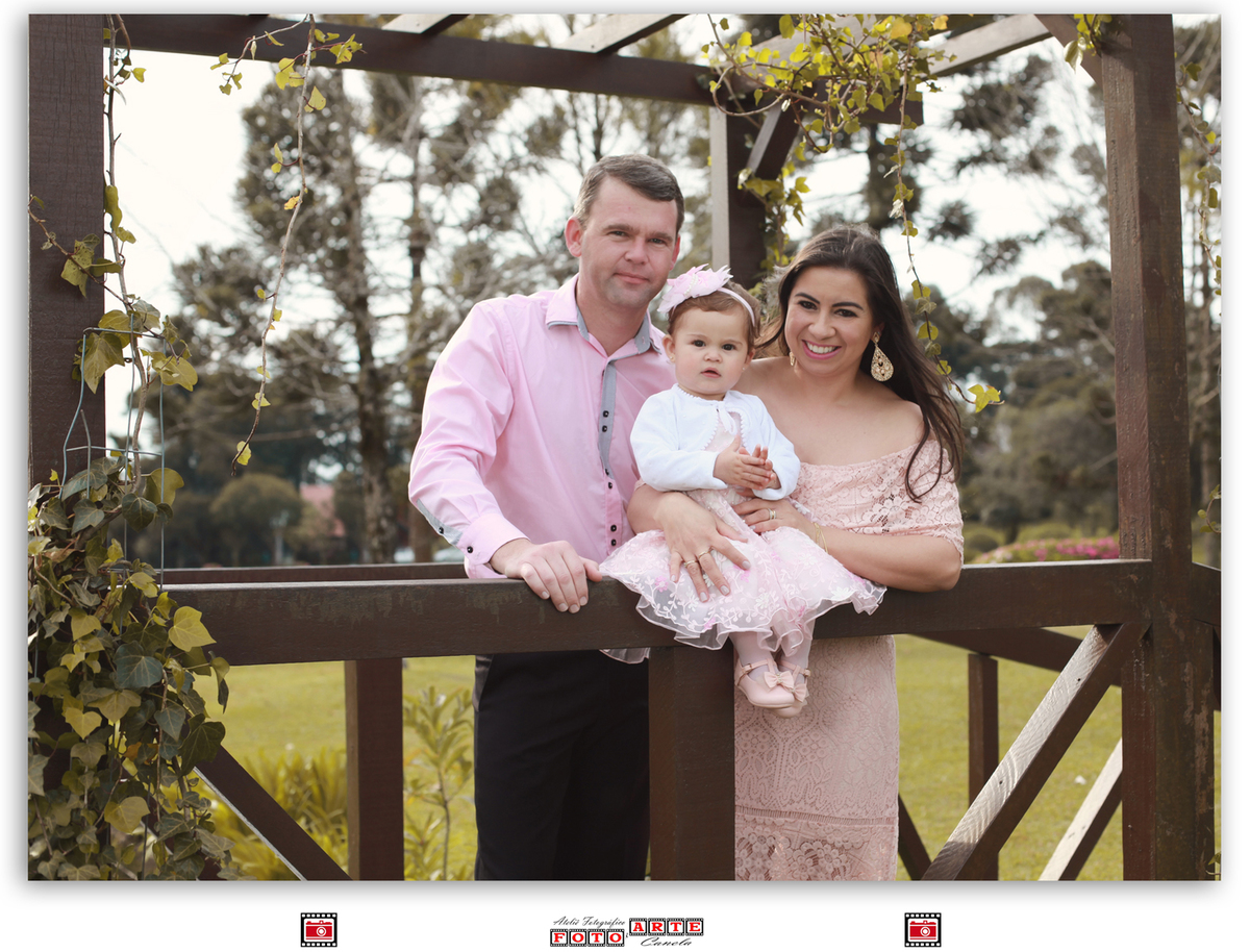 casal de rosa segurando nenê em ponte de madeira
