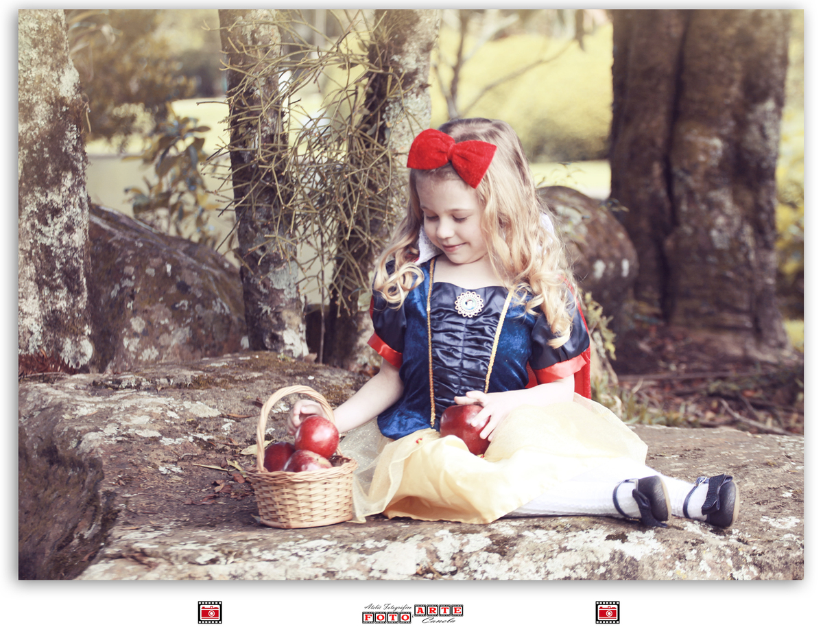 menina sentada com vestido da branca de neve olhando para maçãs