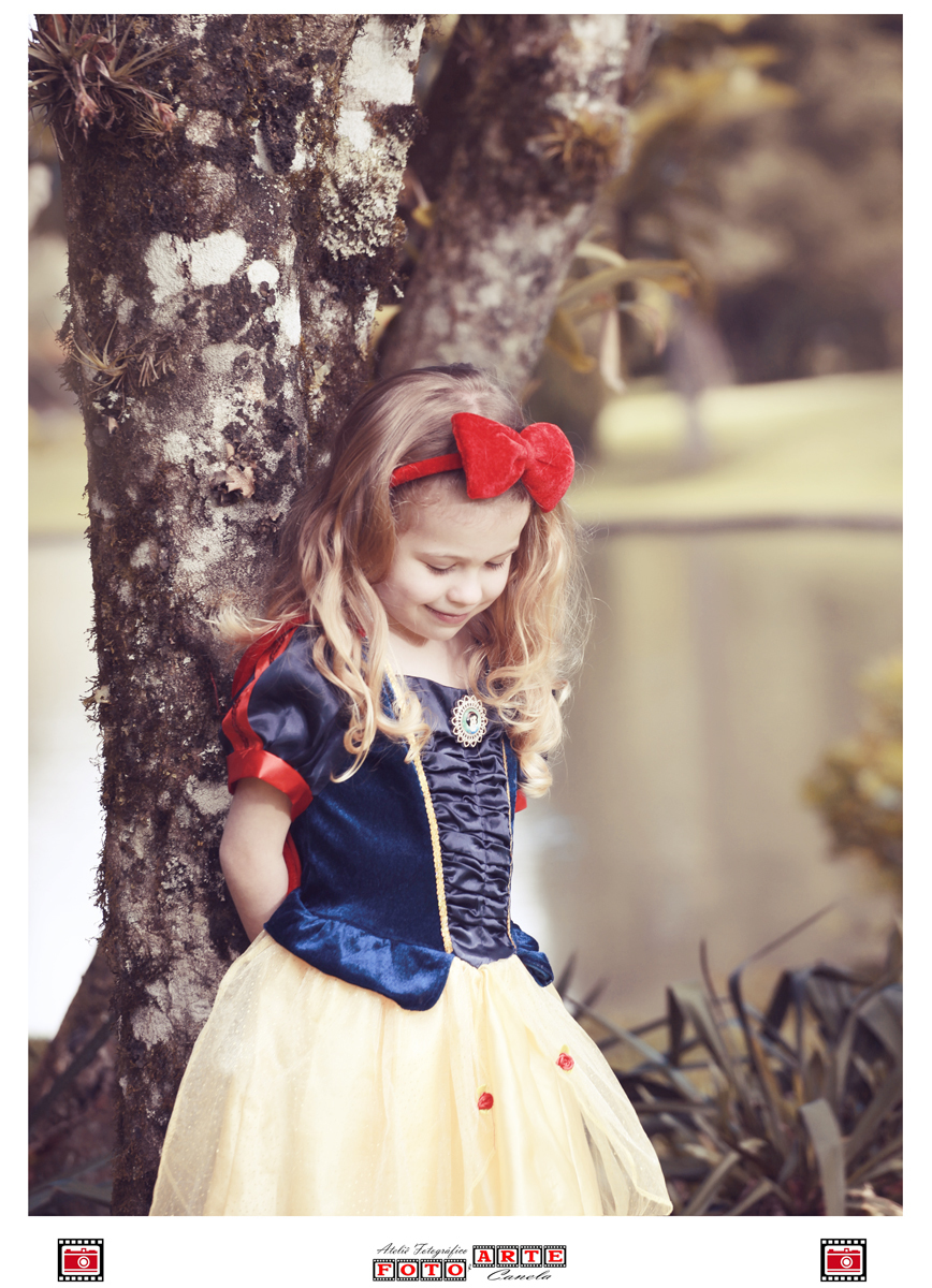 menina com vestido da branca de neve escorada em árvore e olhando para baixo
