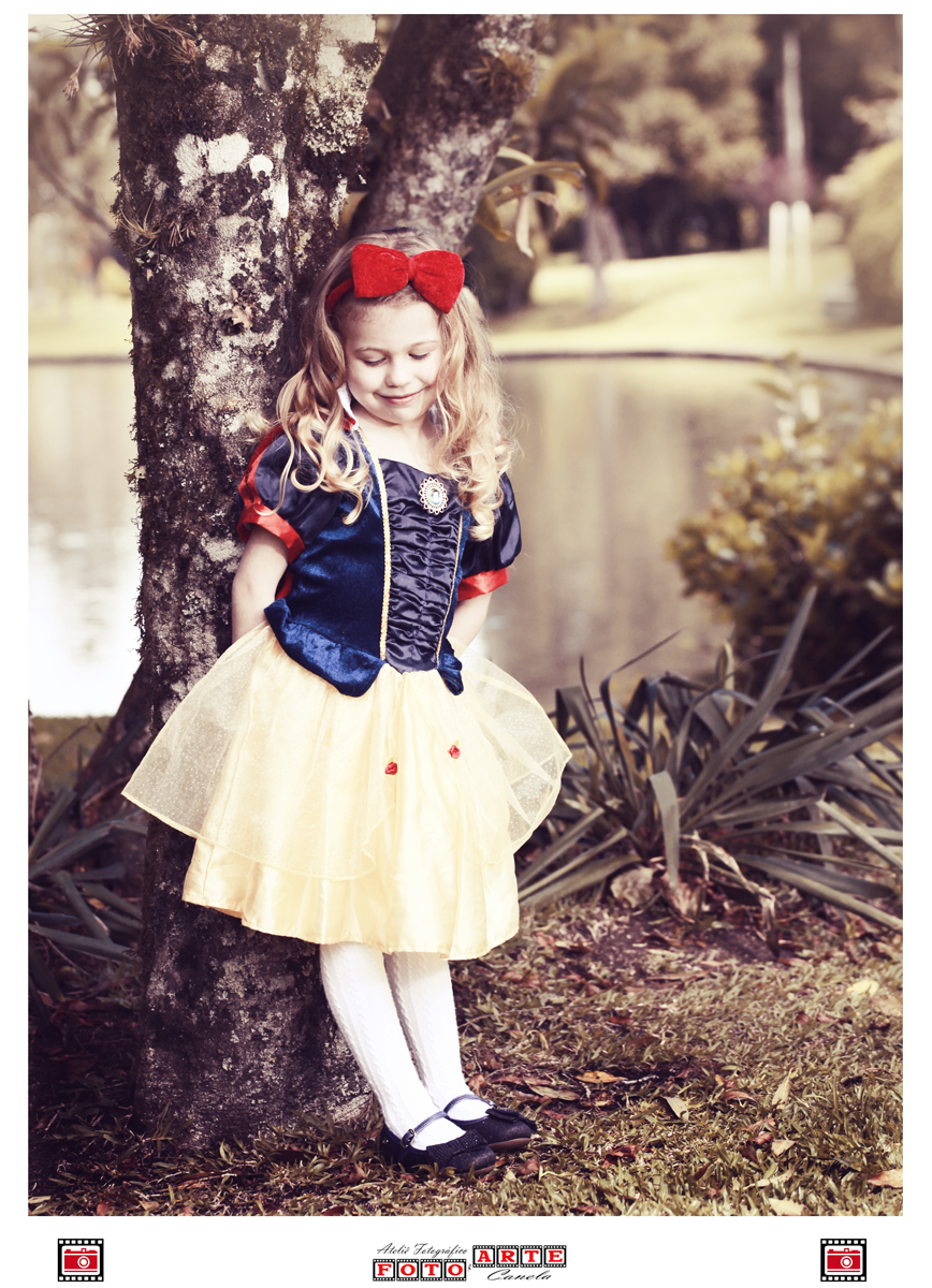 menina escorada em árvore olhando para o chão usando fantasia da branca de neve
