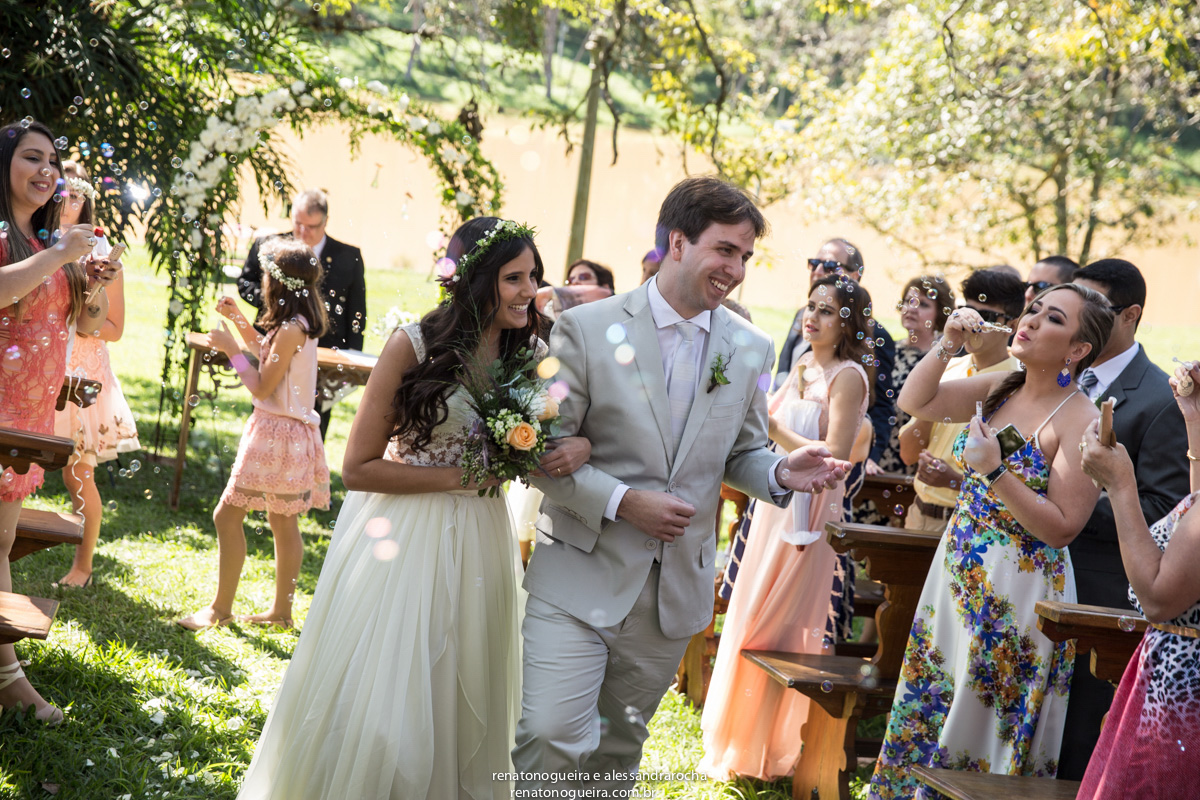 Noivos felizes recebendo homenagem com bolinhas de sabão.
