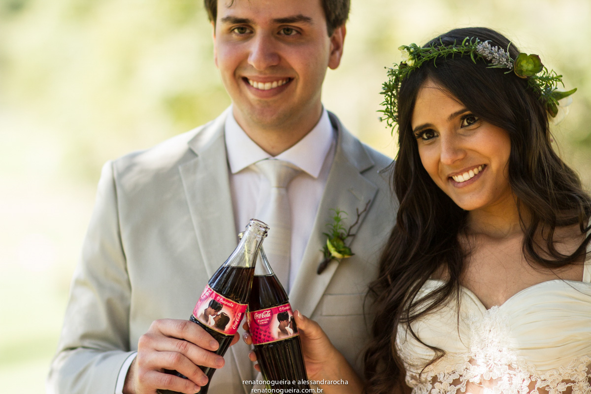 Noivos brindando com garrafa de refrigerante com rotulo com fotos deles.