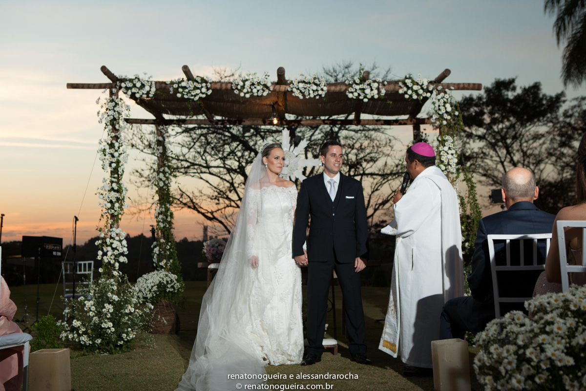Noivos no altar com o padre e o por do sol por traz