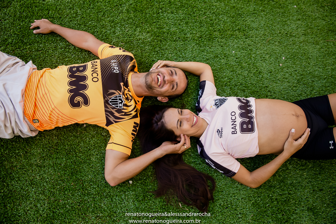 gestante e marido deitados no gramado do mineirão, muito felizes.