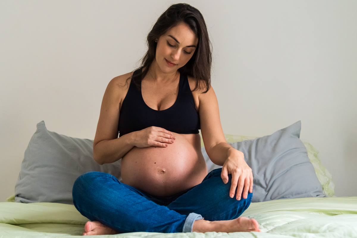 Mariana na cama admirando barriga em ENSAIO GESTANTE EM SÃO PAULO