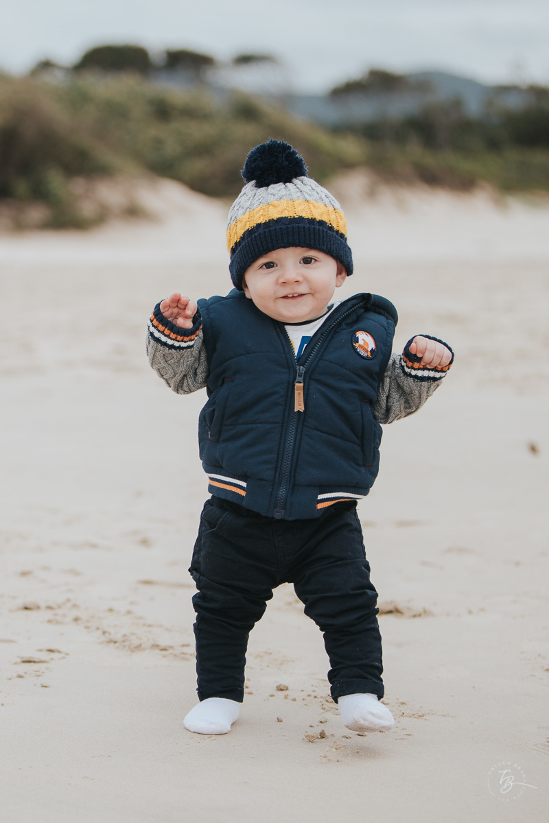 menino de gorro se divertindo na praia em sessao de fotos de familia