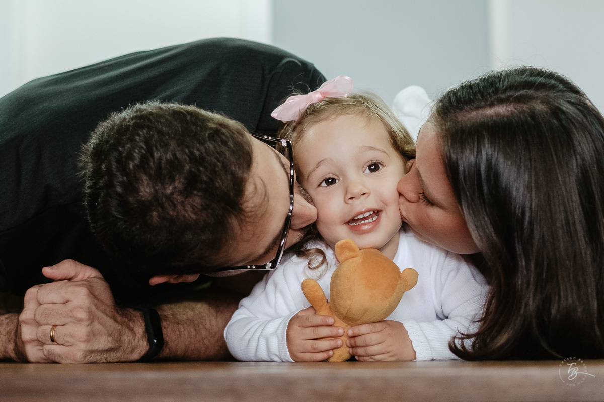 Pai e mãe beijando a filha. Fotografia documental de aniversário infantil em Florianópolis/Sc por Thiago Braga.