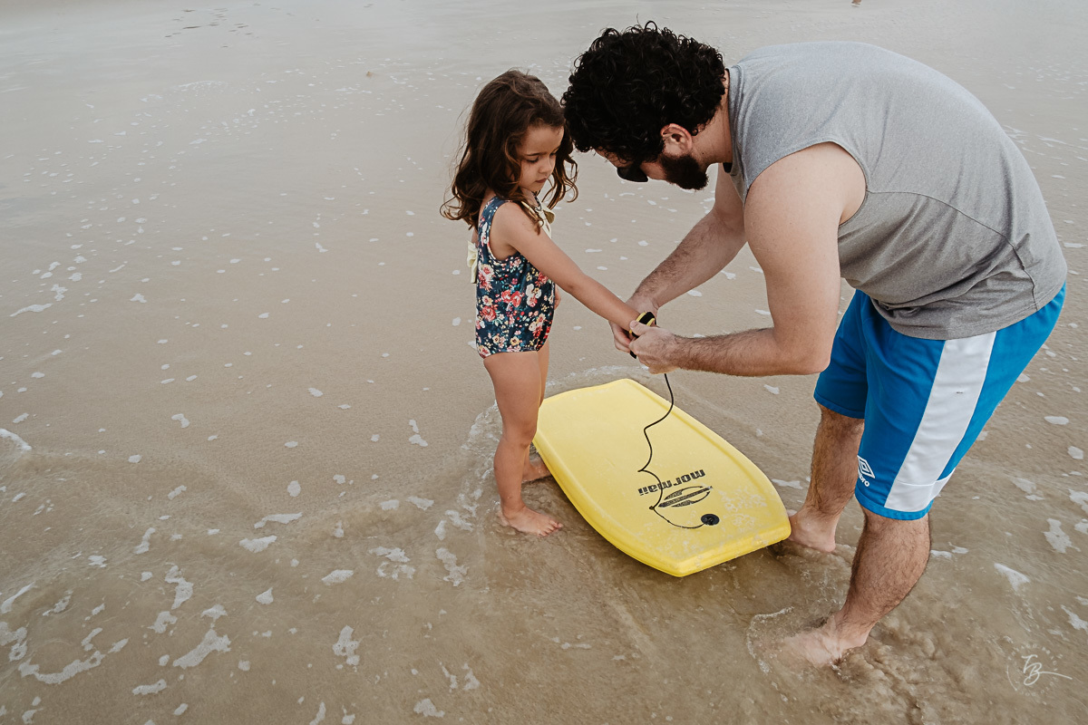 Papai ajudando a pegar onda. Fotografia documental de família. ensaio de família. Praia do Campeche, por Thiago Braga Fotografia. Família Barcarol.