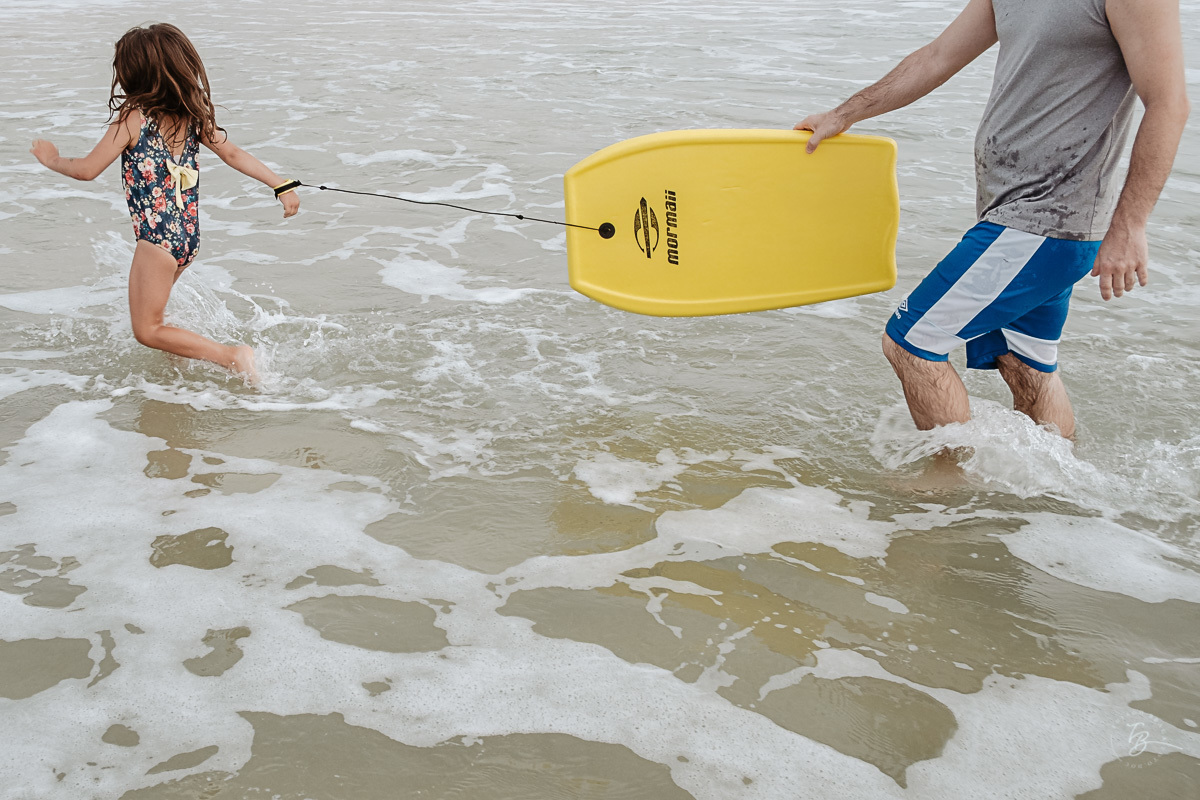 Menina desistindo de pegar onda. Fotografia documental de família. ensaio de família. Praia do Campeche, por Thiago Braga Fotografia. Família Barcarol.