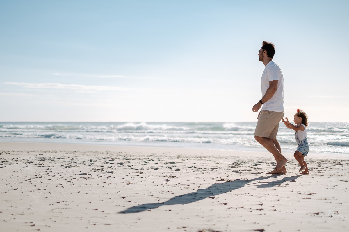 Filha empurrando seu pai. Ensaio lifestyle família, na praia do Santinho em Florianópolis, por Thiago Braga Fotografia. 