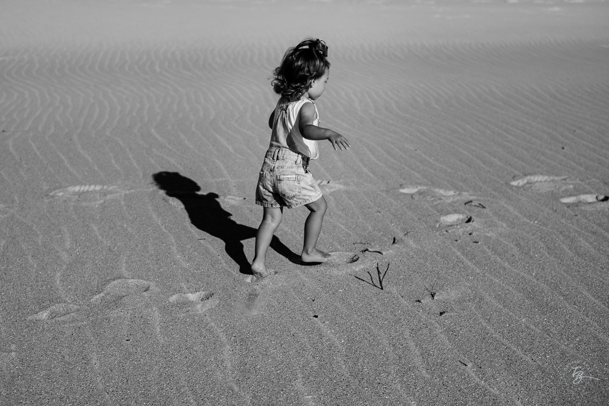 Menina correndo e sua sombra n a areia da praia. Ensaio lifestyle família, na praia do Santinho em Florianópolis, por Thiago Braga Fotografia. 