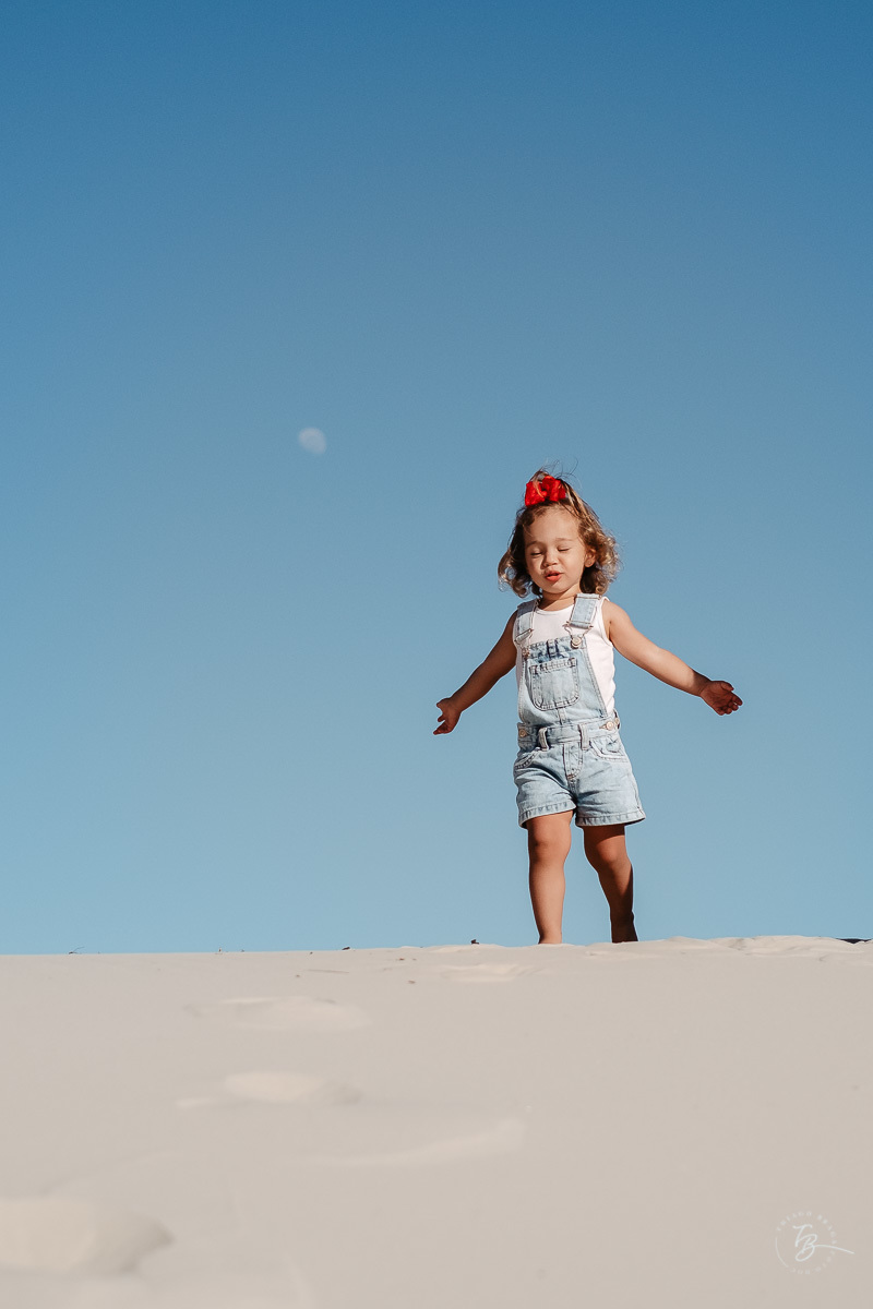 Menina com a lua e céu azul. Ensaio lifestyle família, na praia do Santinho em Florianópolis, por Thiago Braga Fotografia. 