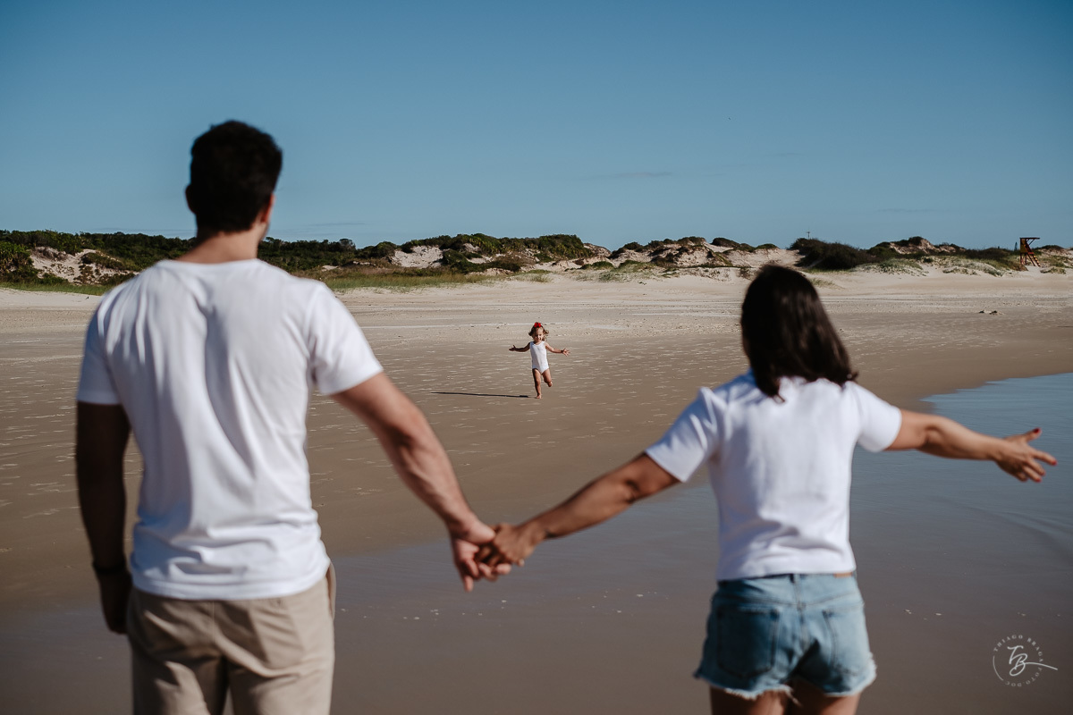 Pais abrindo os braços para sua filha, na praia. Ensaio lifestyle família, na praia do Santinho em Florianópolis, por Thiago Braga Fotografia. 