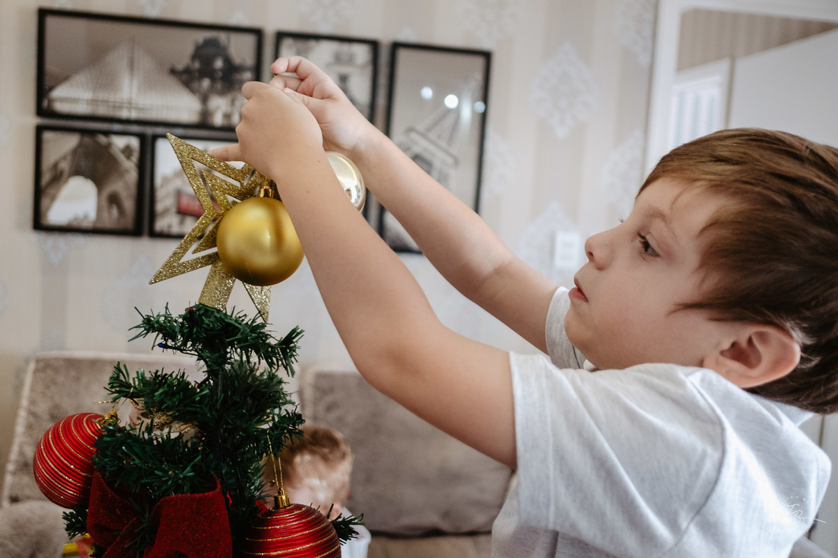 Menino colocando a estrela na árvore de natal. Ensaio de natal em casa por Thiago Braga Fotografia.