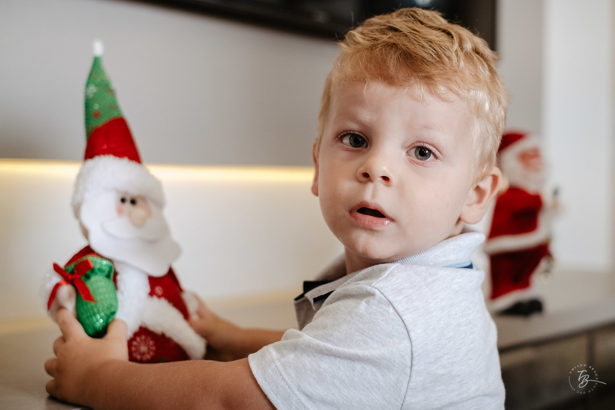 Menino com enfeite do papai Noel. Ensaio de natal em casa por Thiago Braga Fotografia.