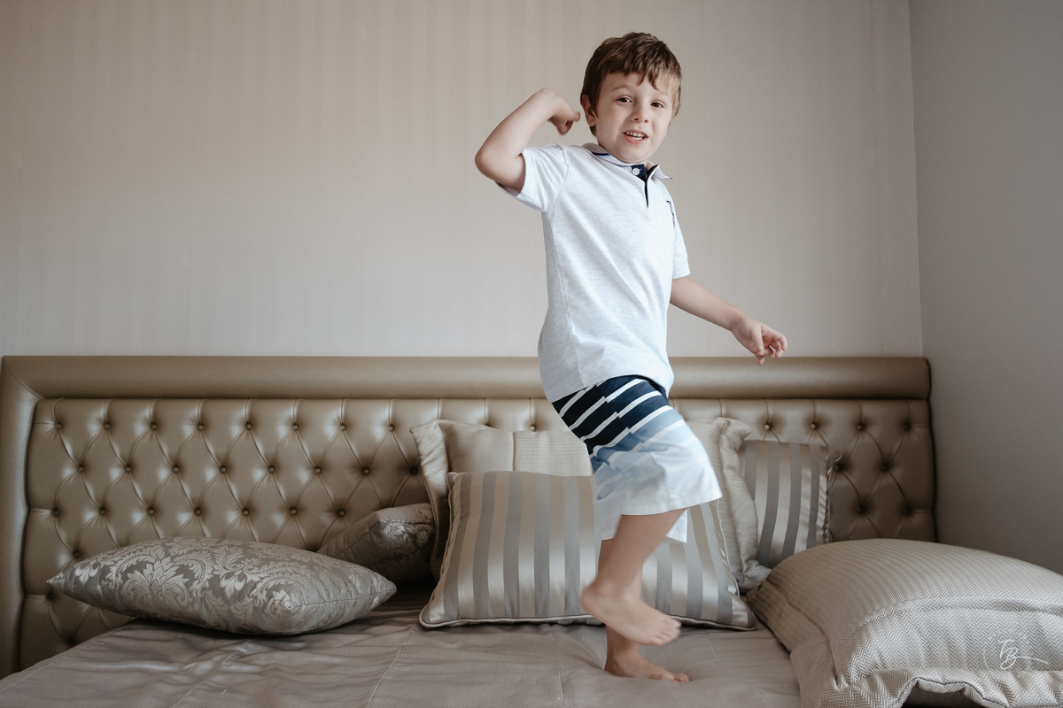 Menino pulando na cama de casa. Ensaio de natal em casa por Thiago Braga Fotografia.