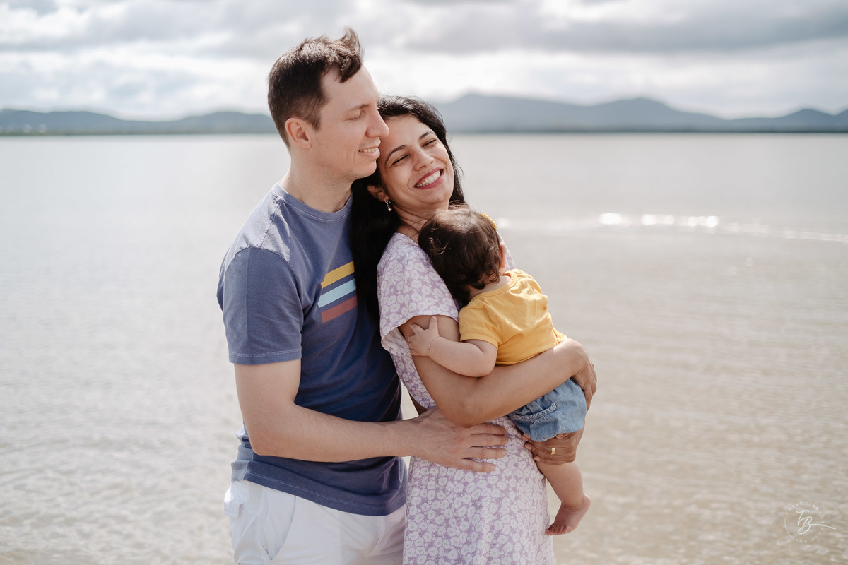 Bebê dormindo no coloc da mãe e pai. Ensaio de família. Acompanhamento do primeiro aninho da Khloe. Praia da Daniela em Florianópolis/SC, por Thiago Braga Fotografia. 