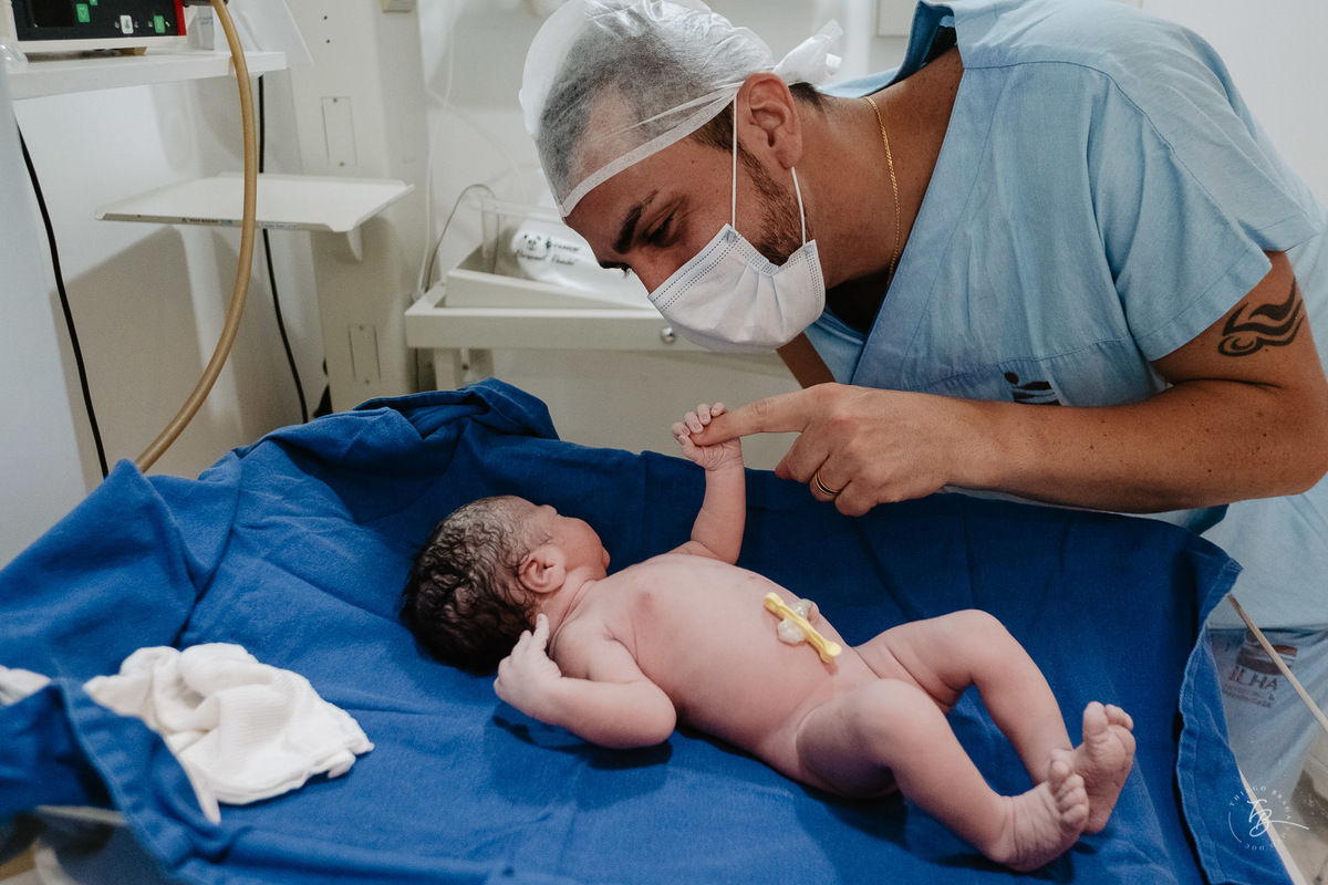 Dedo do papai na mãozinha da sua filha recém nascida. Parto cesárea na maternidade Ilha, em Florianópolis, por Thiago Braga Fotografia.