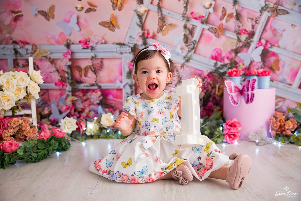 Bebê sorrindo para a foto com o número um no cenário de jardim com borboletas