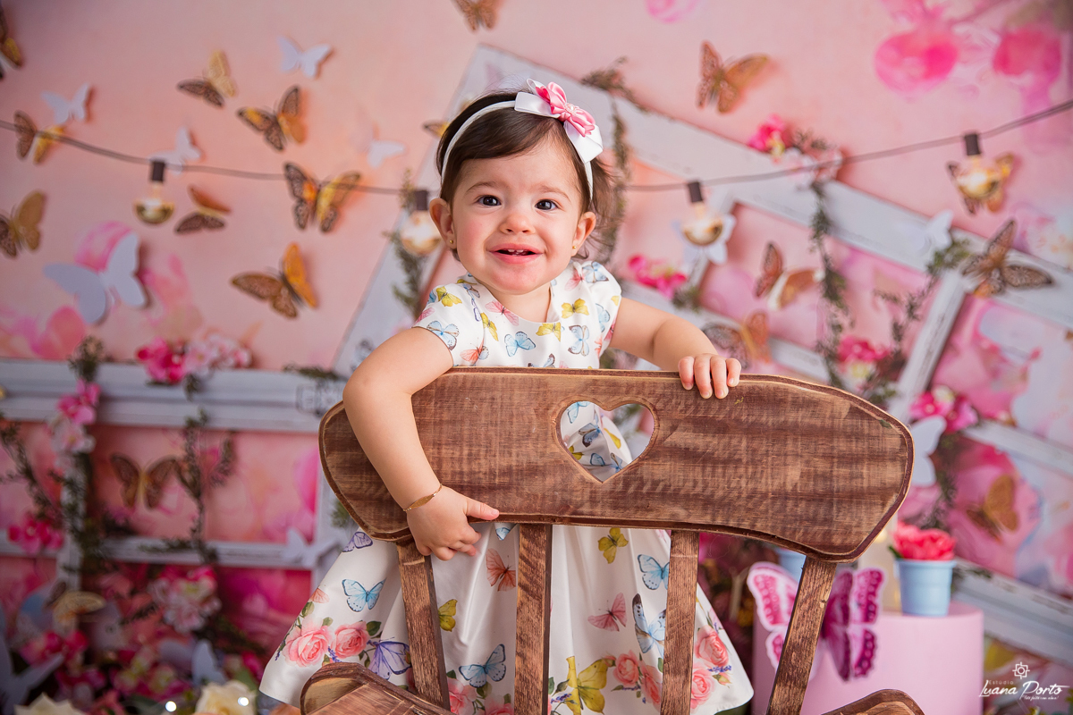 Bebê menina com tiara no cabelo em pé num cenário de fotos de borboletas
