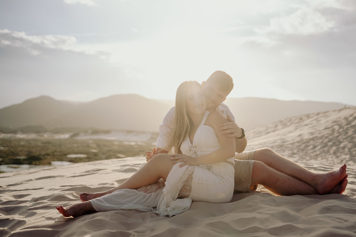 foto de pre wedding feita nas dunas com por do sol. casal sentado na areia namorando. foto feita por javorski producoes