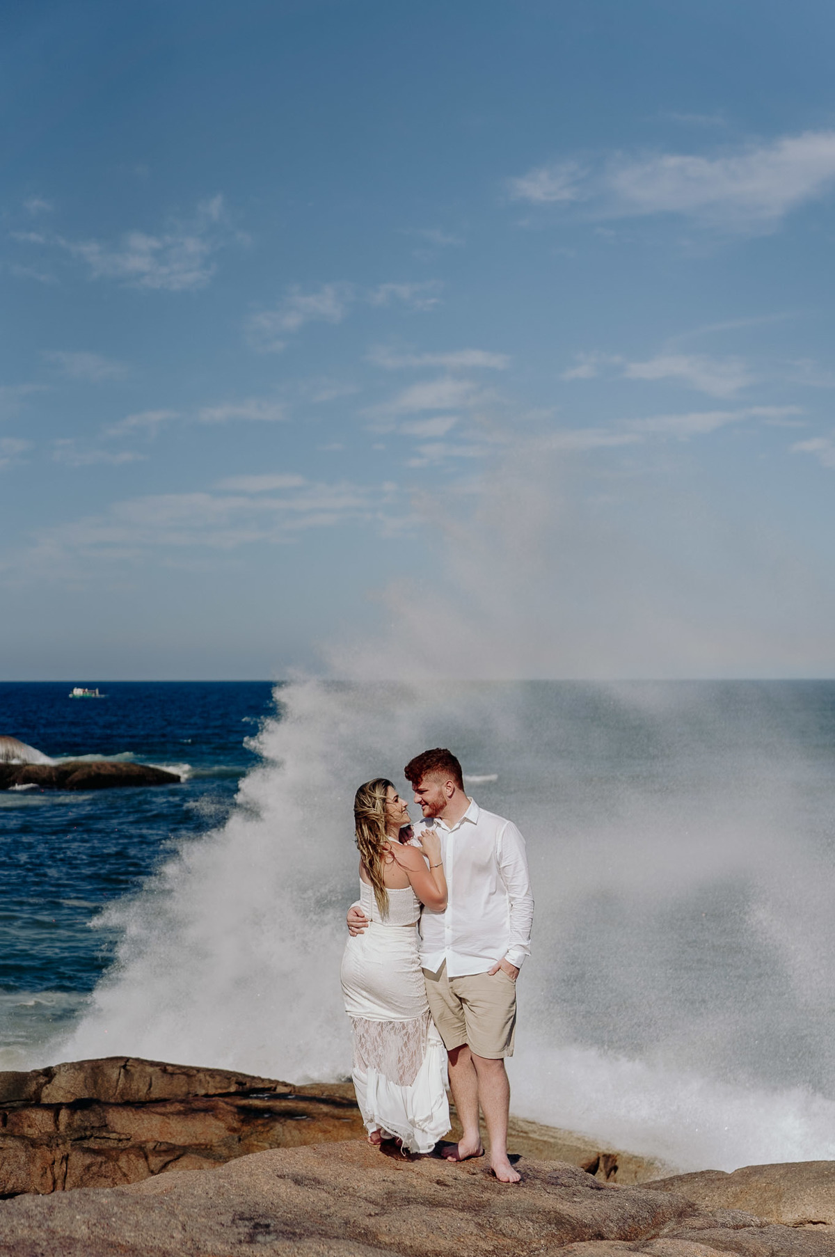 Foto pré wedding na praia, com onda estourando atrás do casal. dia de fotos com muito calor. foto feita por Javorski Producoes