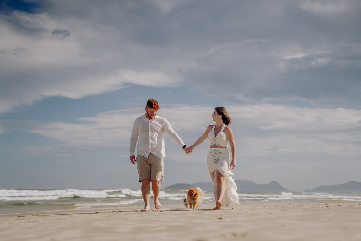 foto de pre wedding feito na praia com cachorros. casal andando na praia com cachorro e casal muito feliz. foto feita por javorski producoes 
