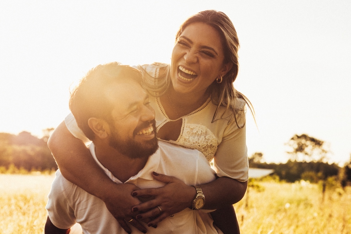 casal feliz sorrindo noiva nas costas do noivo por do sol