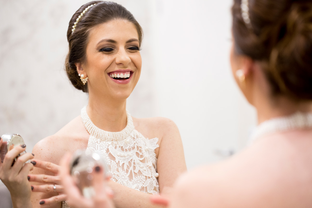noiva sorrindo ao olhar no espelho em seu make up realizado pelo maquiador Cris Rozzini no casamento de Eliete e Matheus.