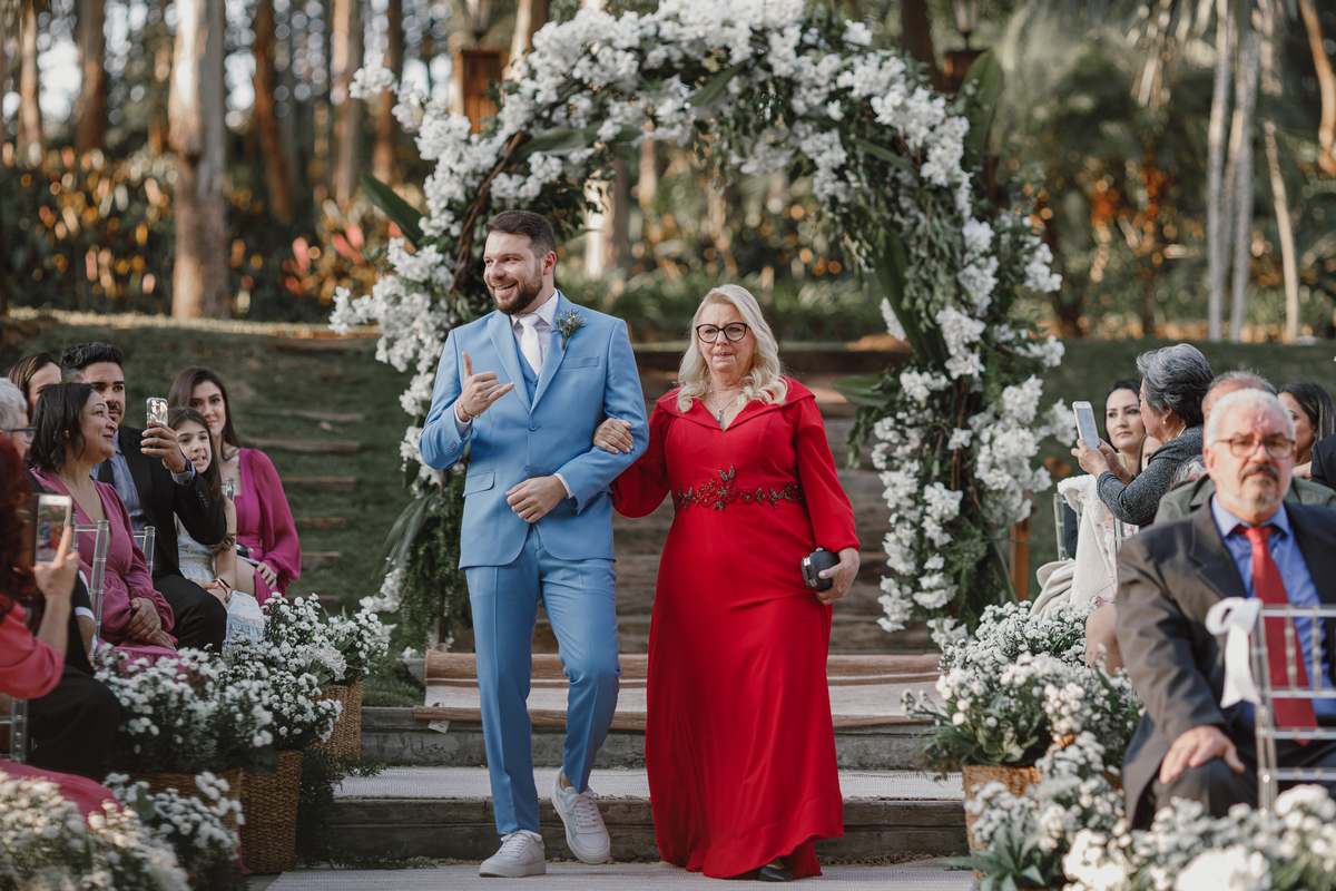 entrada do noivo com a mãe no casamento cerimônia externa arco de flores brancas