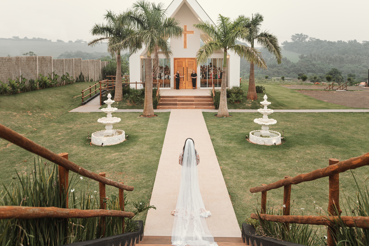 entrada de noiva na capela chácara Lalinda Maringá e região noiva com véu longo caminahndo em direção a porta