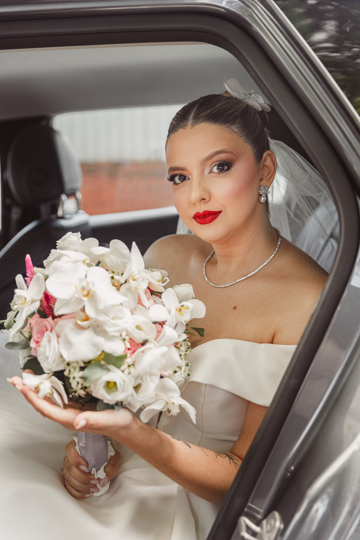 retrato da noiva no carro com buquê noiva de batom vermelho e penteado preso buquê branco fotografo de casamentos