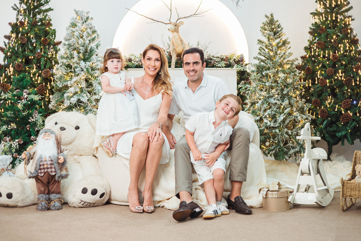 Pais e filhos durante ensaio fotográfico de Natal em estúdio com cenário iluminado e decoração natalina.
