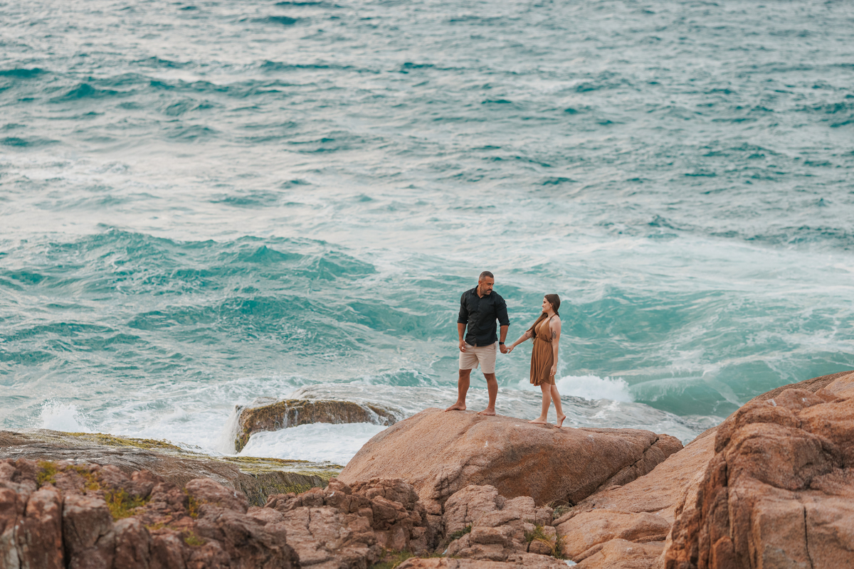Fotografia de casal em meio às pedras e ao mar
