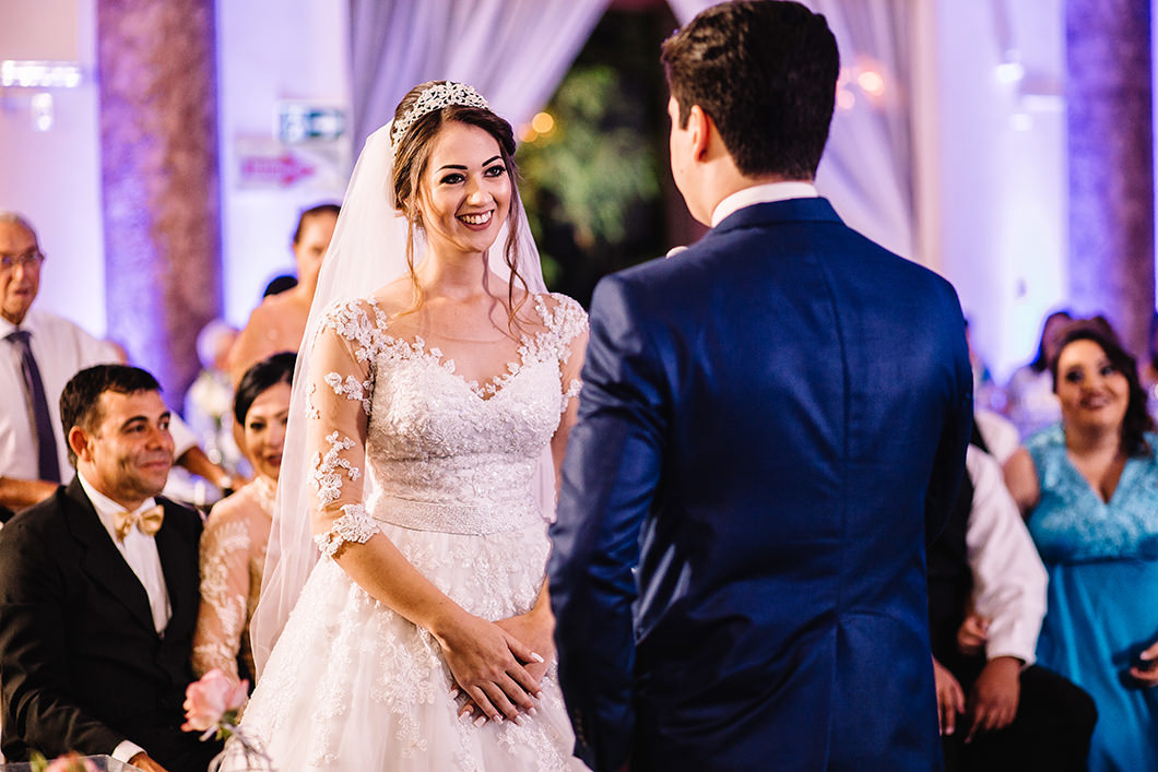 Foto da noiva ouvindo votos de casamento do noivo