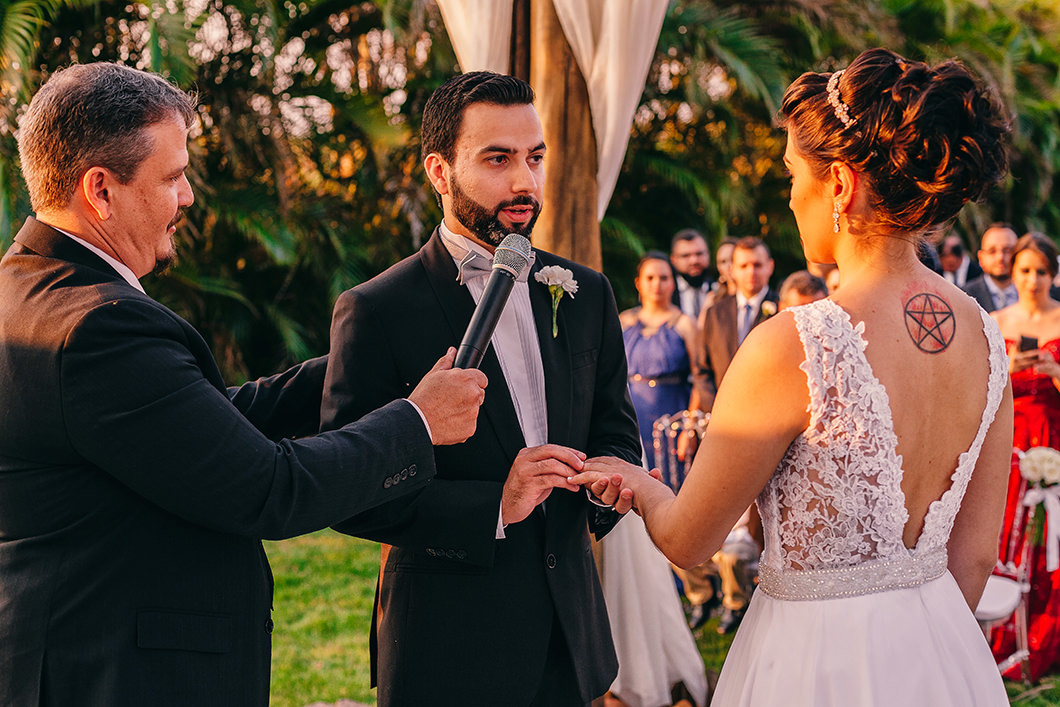 Foto de casamento noivo colocando aliança na noiva em Casamento ao ar livre 