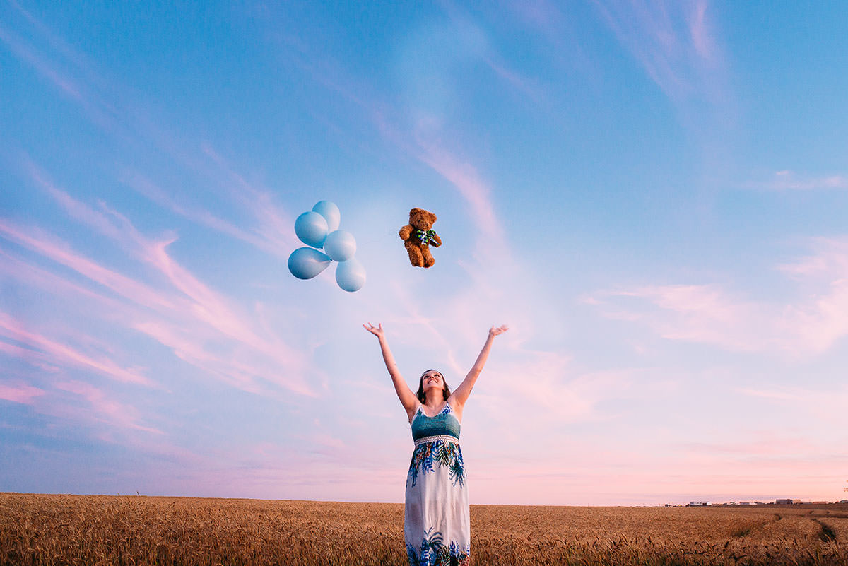 gestante jogando ursinho pra cima junto com baloes no trigo